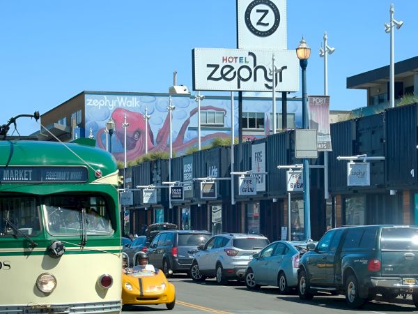A green vintage streetcar/vehicle sits in traffic outside Hotel Zephyr, with the ZephyrWalk sign and storefronts behind.