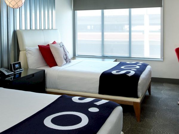 Modern hotel room with two twin beds, red chairs, a desk, and a window with blinds.