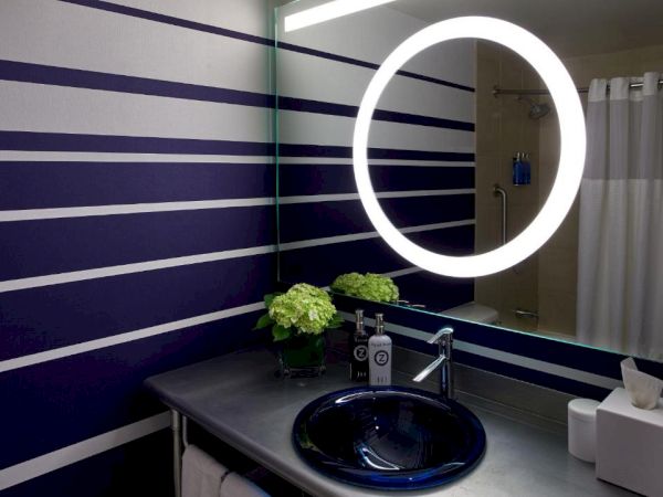 A modern bathroom vanity with a striped wall, a glowing ring-lit oval mirror, and a blue sink basin.