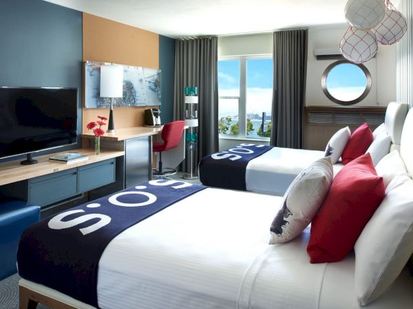 Modern hotel room with a bed, TV console, curtains, window view, and red/white hanging sphere lights.
