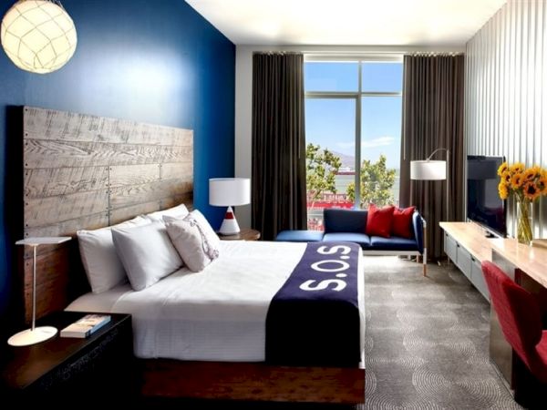 Bright modern bedroom with a blue accent wall, large bed, curtains, big window, and sunflowers on the dresser.