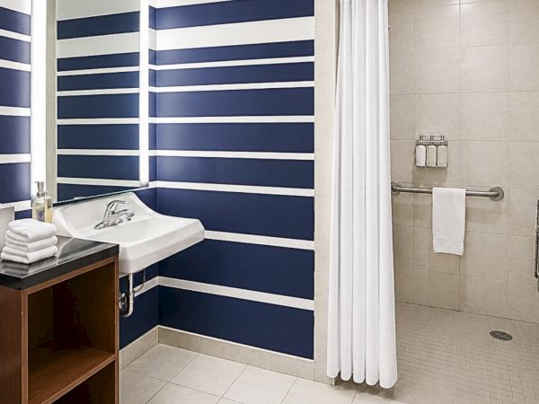A modern blue-and-white bathroom with a sink, folded towels, and a tiled shower area with grab bars.