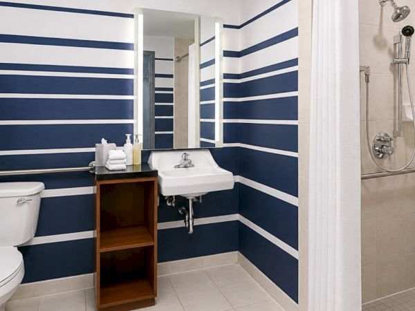 A modern bathroom with striped blue-and-white walls, toilet, sink vanity, and a shower with fixtures and towel.