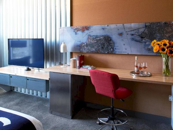 An office suite: wooden desk with a red chair, monitor, world map wall art, wine glasses, and bright sunflowers.