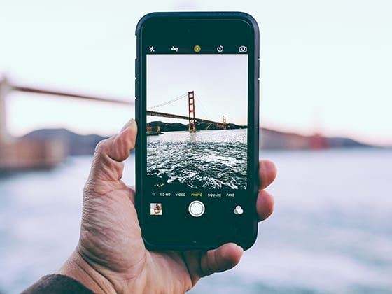 Hand holding a phone photographing the Golden Gate Bridge