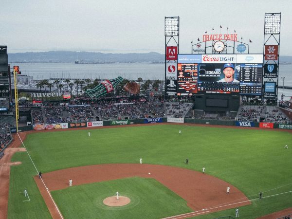 A packed baseball stadium, Oracle Park in San Francisco, with fans and giant ads over the outfield.